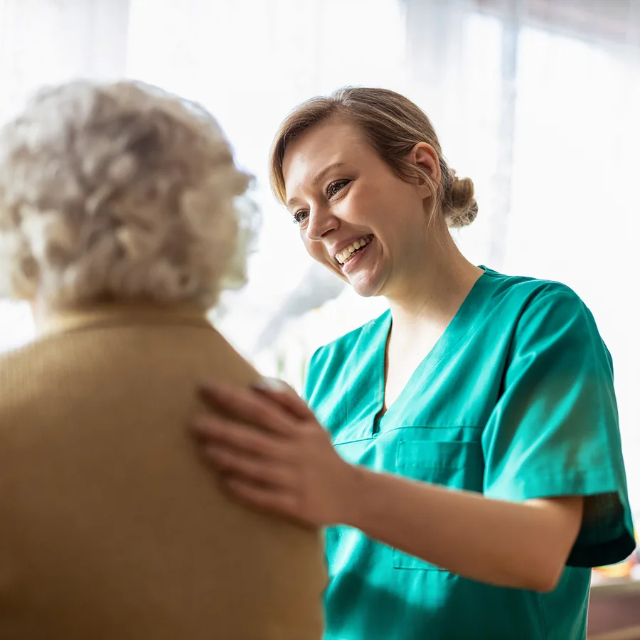 Clinician in teal scrubs smiling while assisting an older patient